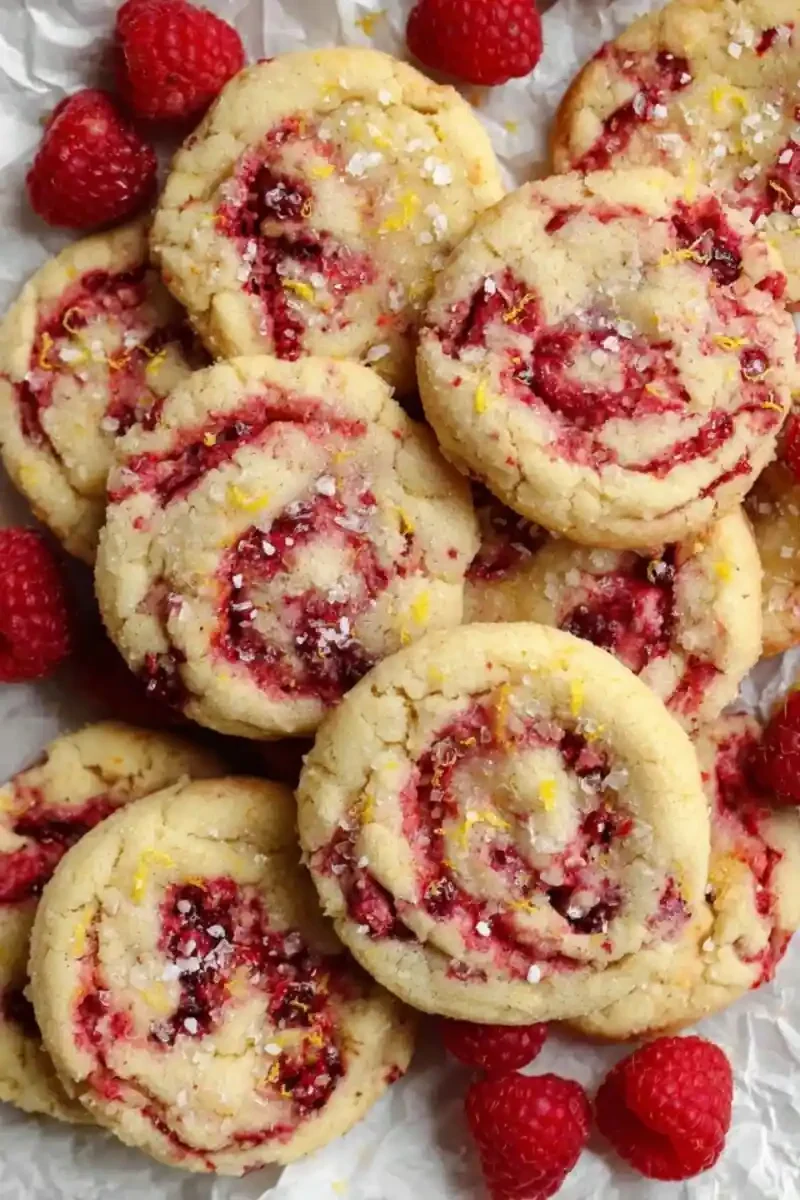Soft lemon raspberry cookie with a bite taken out, swirled with vibrant raspberries and topped with sugar and lemon zest