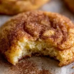 Close-up of a soft snickerdoodle cookie with a bite taken, showing a moist, fluffy interior coated in cinnamon sugar