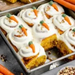 Frosted carrot cake cinnamon rolls in a baking pan topped with cream cheese icing and decorative fondant carrots