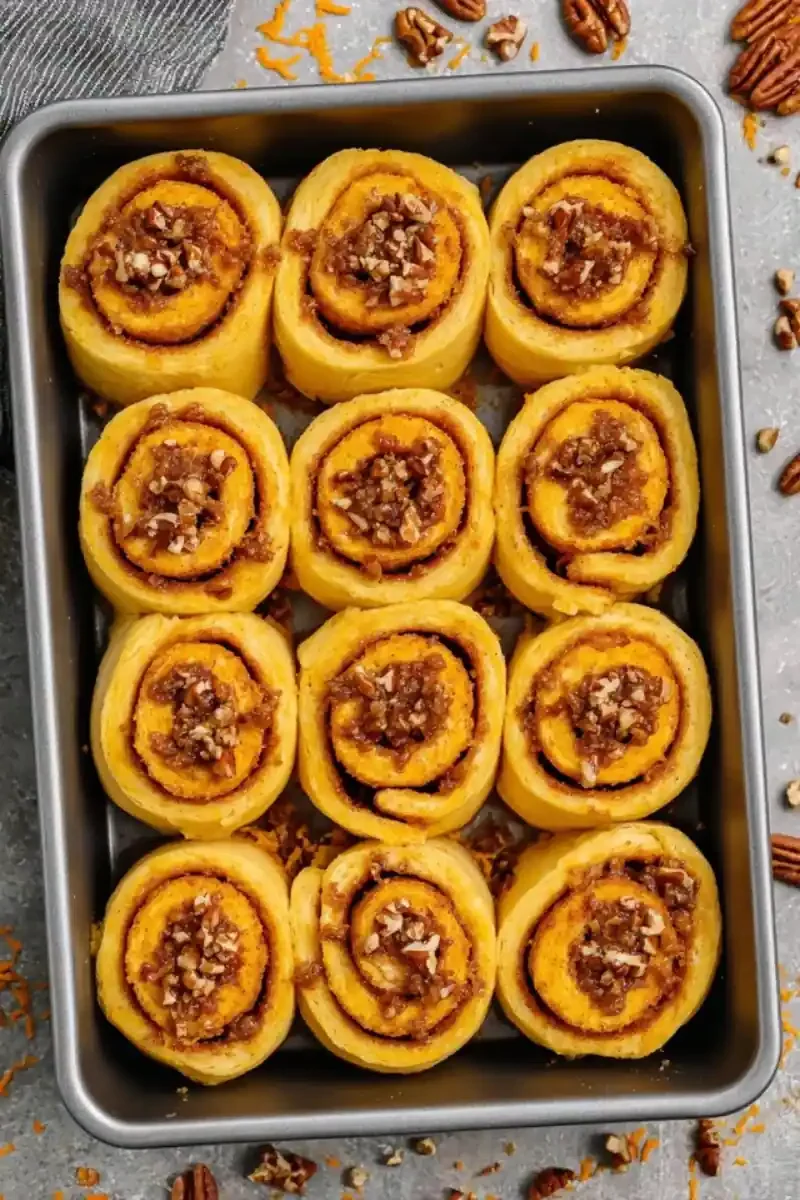 Freshly baked carrot cake cinnamon rolls topped with chopped pecans in a baking pan