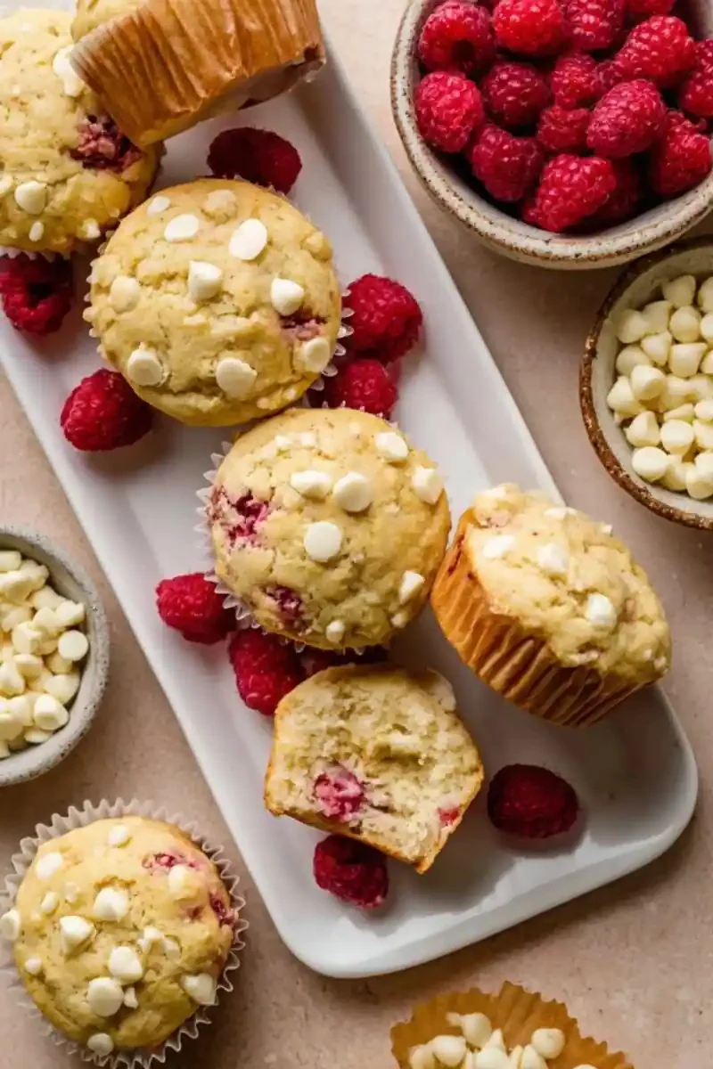 Homemade white chocolate raspberry muffins served with fresh raspberries and white chocolate chips on a tray